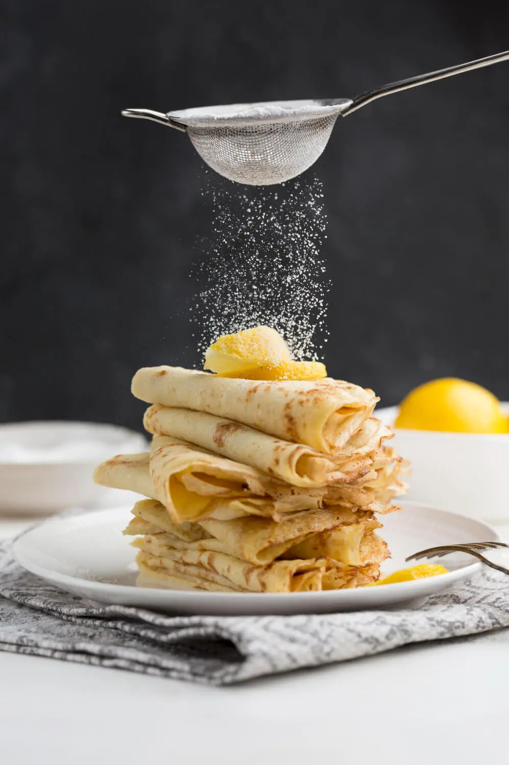 Thin crepes dusted with powdered sugar, stacked and topped with butter and lemon