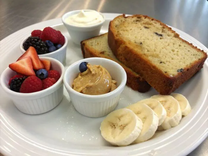 Banana bread slice on a plate with cream cheese, peanut butter, and fresh berries on the side