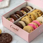 A pink Crumbl box filled with colorful cookies on a marble surface.